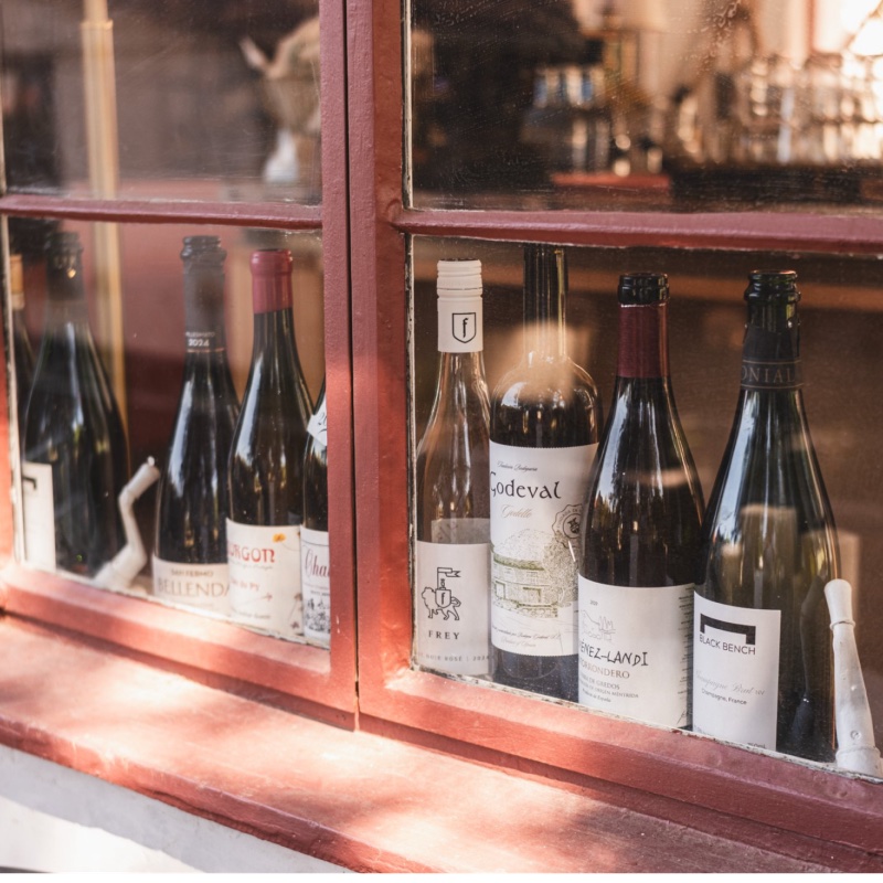 Bottles of wine lined up in a red-framed window