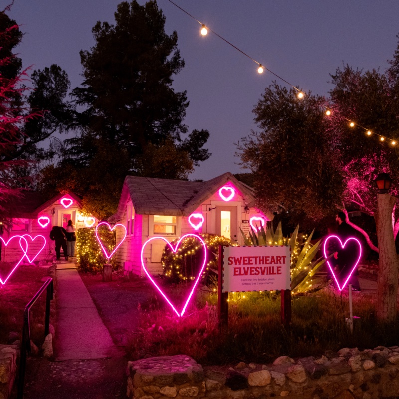 Cottages glowing with pink neon hearts beside a Sweetheart Elvesville sign