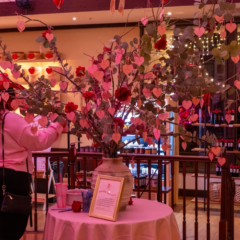 A guest hanging a handwritten heart tag on a tree of roses and paper hearts